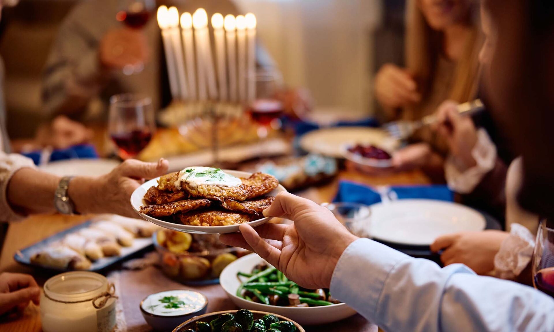 Close-up of a family at a dinner table featuring Hanukkah foods, including latkes and other signature fried cuisine.