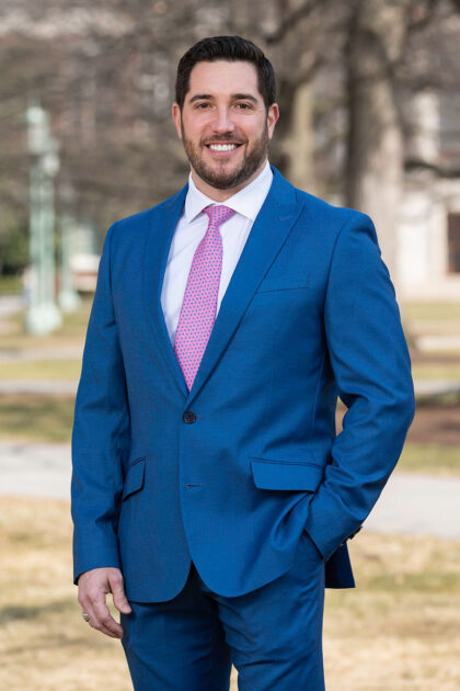 Vertical portrait of Robert Alexander in a blue suit outside. 