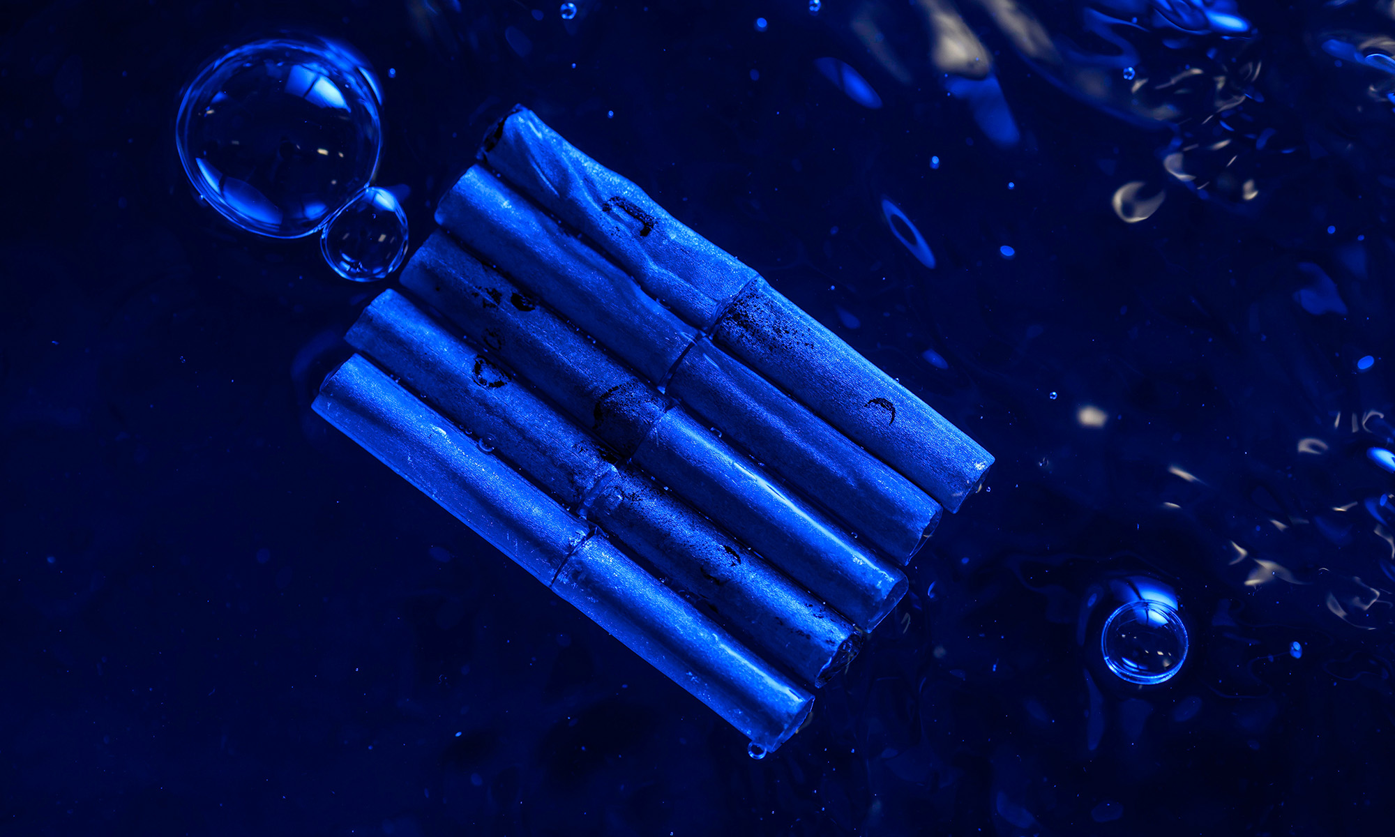 Five unsinkable metal tubes bound together and seen from above floating in water with bubbles nearby and an overall blue cast.