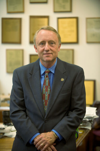 Kevin Parker seated on his desk with his hands folded in front of him and smiling at the camera.