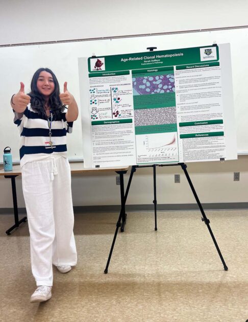 Norah DeMayo smiles and gives a double thumbs up standing next to her poster presentation during the University of Rochester's Pre-College Summer Program courses.