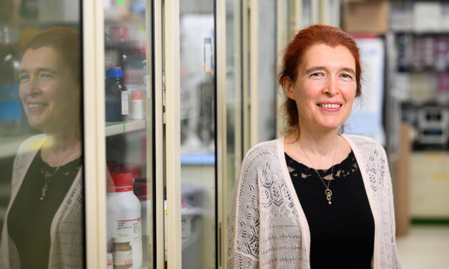 Vera Gorbunova smiles at the camera with her reflection in the cases of her lab.