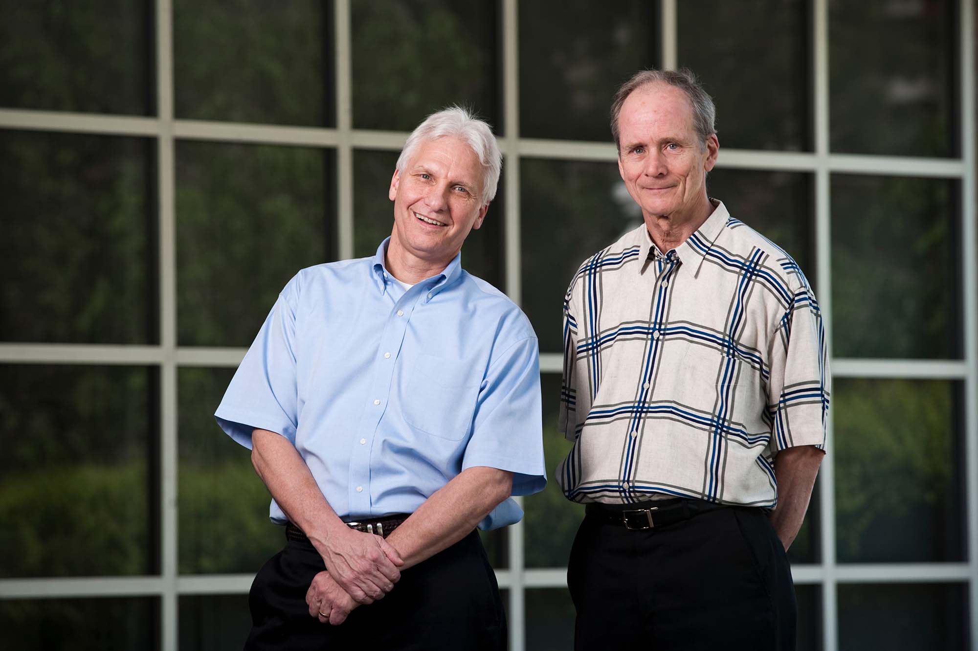 Richard Ryan and Edward Deci smile at the camera in front of Meliora Hall.