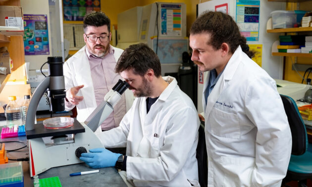 Isaac Harris and two lab members studying glutathione samples with a microscope.