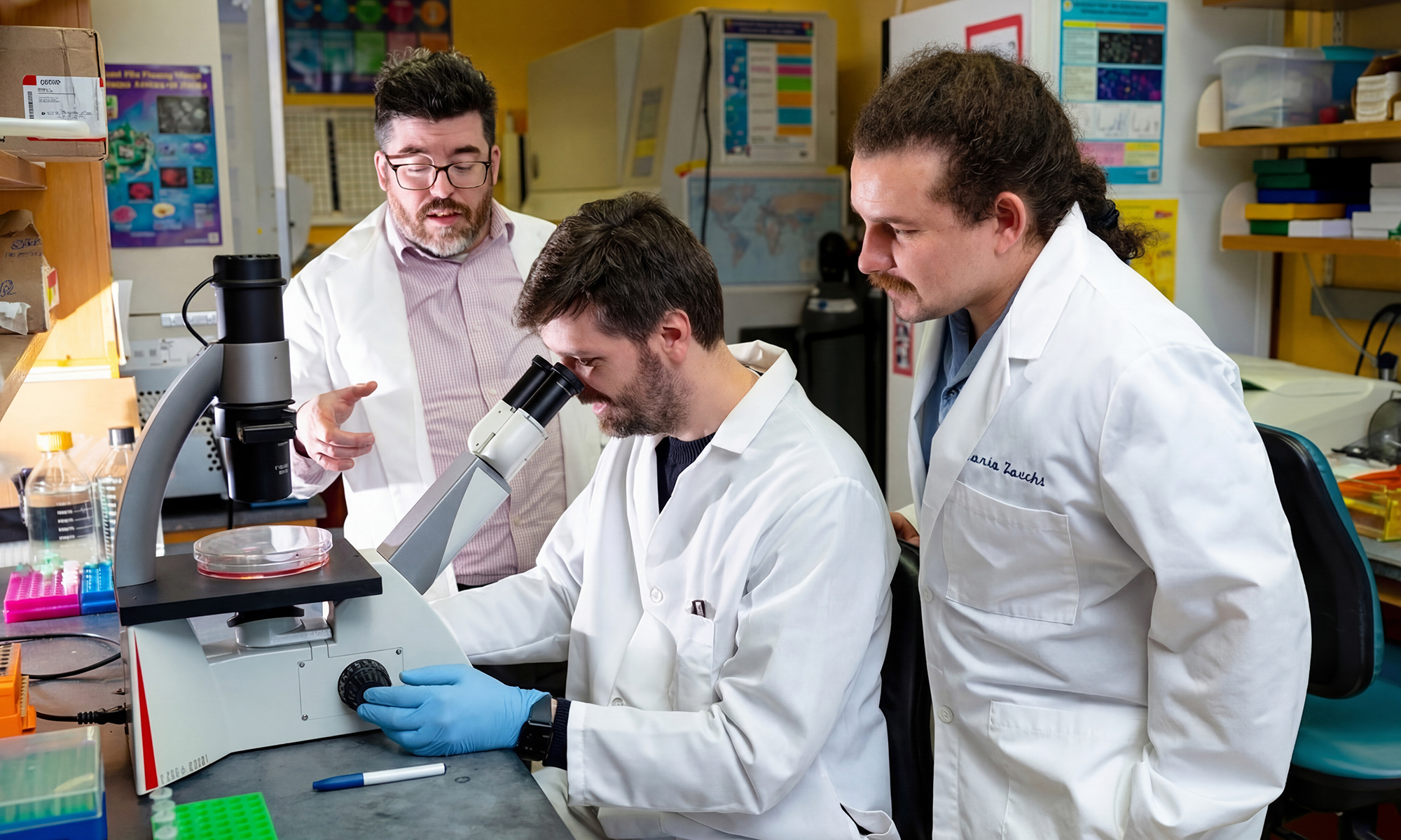 Isaac Harris and two lab members studying glutathione samples with a microscope.