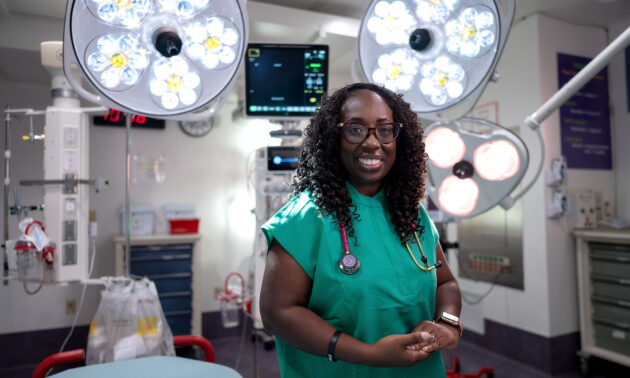 Sylvia Owusu-Ansah outfitted in medical scrubs smiling at the camera while in an emergency room.