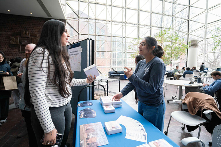 Two people having a conversation over a table of Wilson Commons celebration materials.