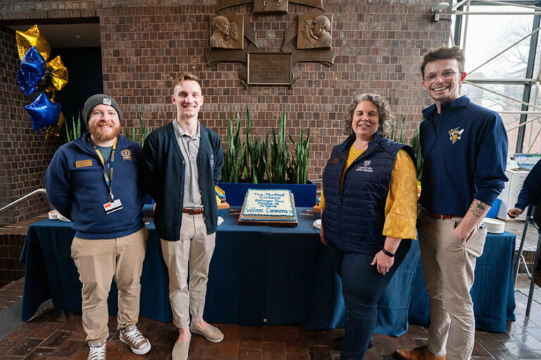 Four Wilson Commons staff members smile while standing next to a birthday cake noting the building's 50th anniversary.
