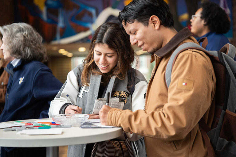 Two University of Rochester students at a high table fill out cards about Wilson Commons during the 50th anniversary celebration.