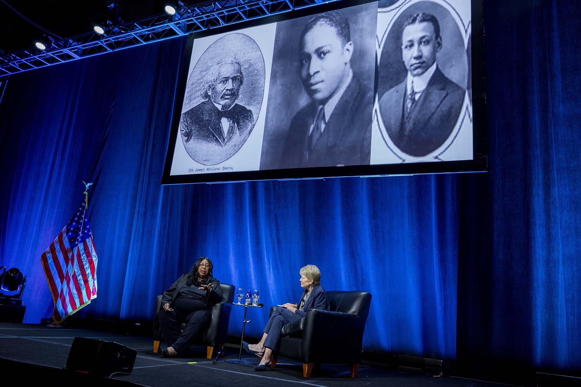 Harriet Washington and Sarah Mangelsdorf seated on stage below a triptych featuring black-and-white photos of Rudolph Fisher, James McCune Smith, and Louis Wright.