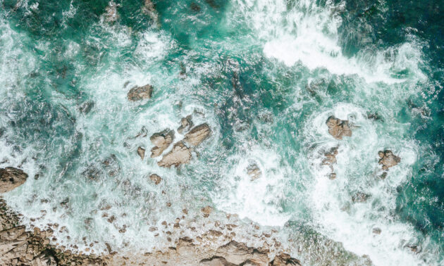 Aerial view of ocean waves swirling over rocks.