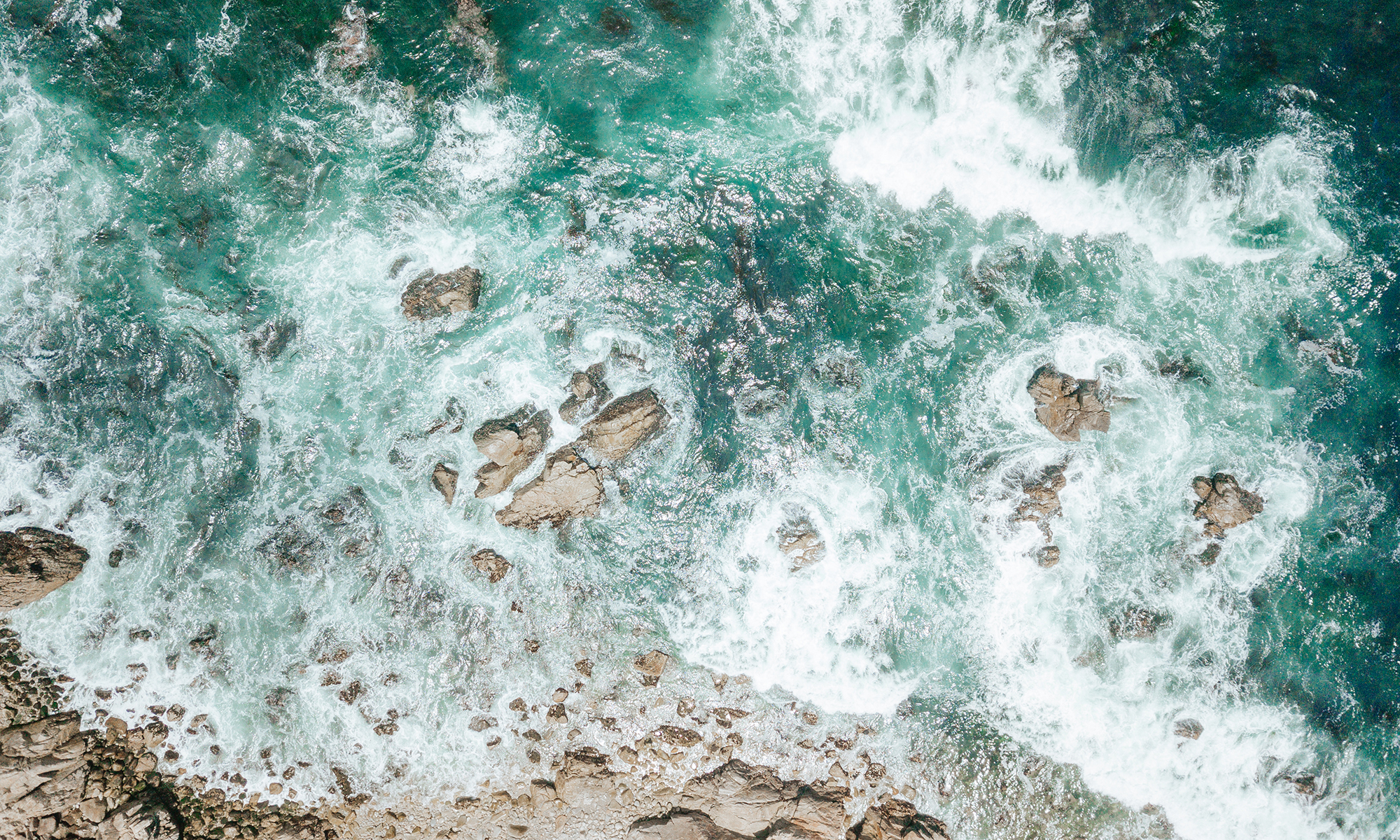 Aerial view of ocean waves swirling over rocks.