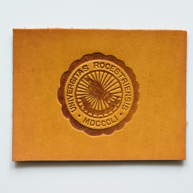 Leather rectangle stamped with the University of Rochester's pre-1928 seal.