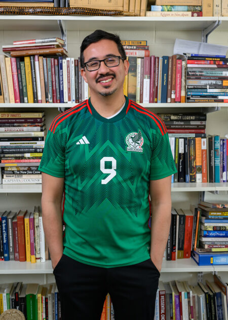 Pablo Sierra Silva in a green Mexico number 9 jersey, smiling in front of his office bookshelves. 