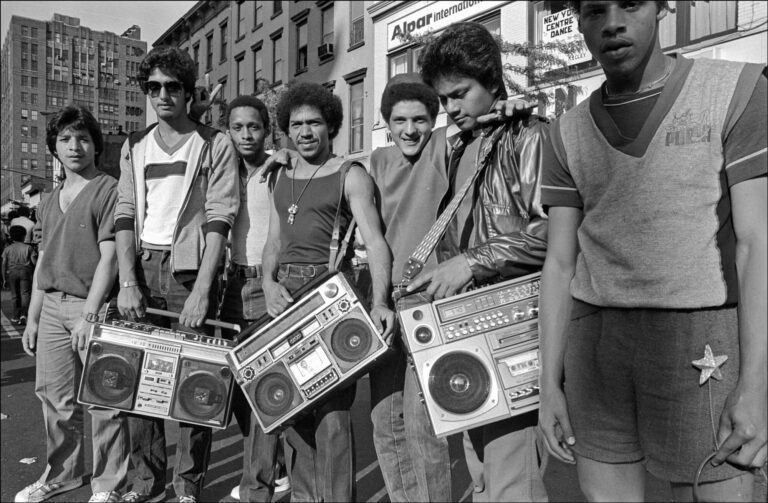 A group of young men stands in front of several boomboxes, showcasing a vibrant music culture.