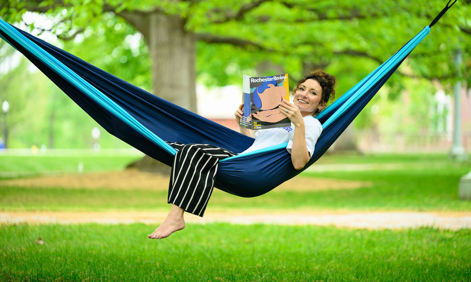 Michelle Kleinhammer in a hammock smiling and reading the spring 2026 issue of Rocheter Review.