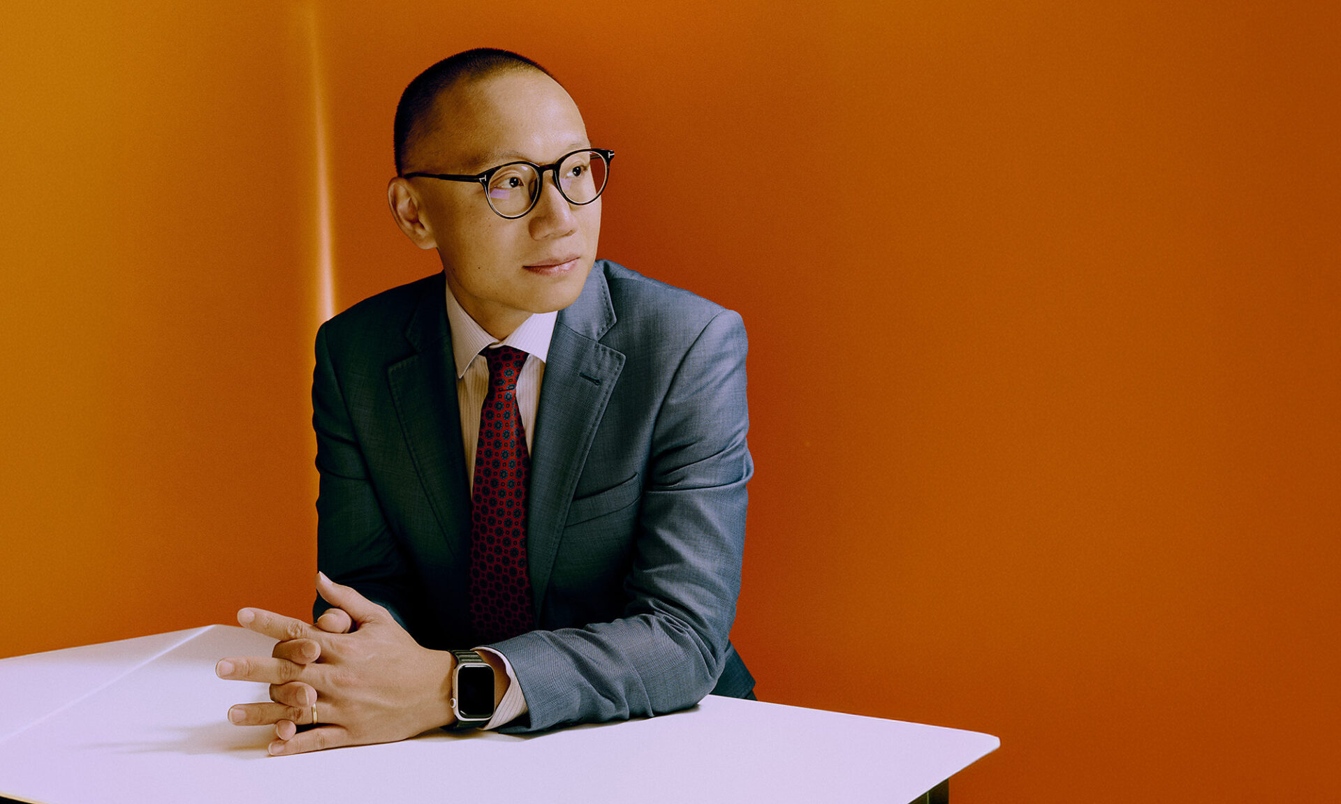 Dan Wang seated at a table in front of an orange background.