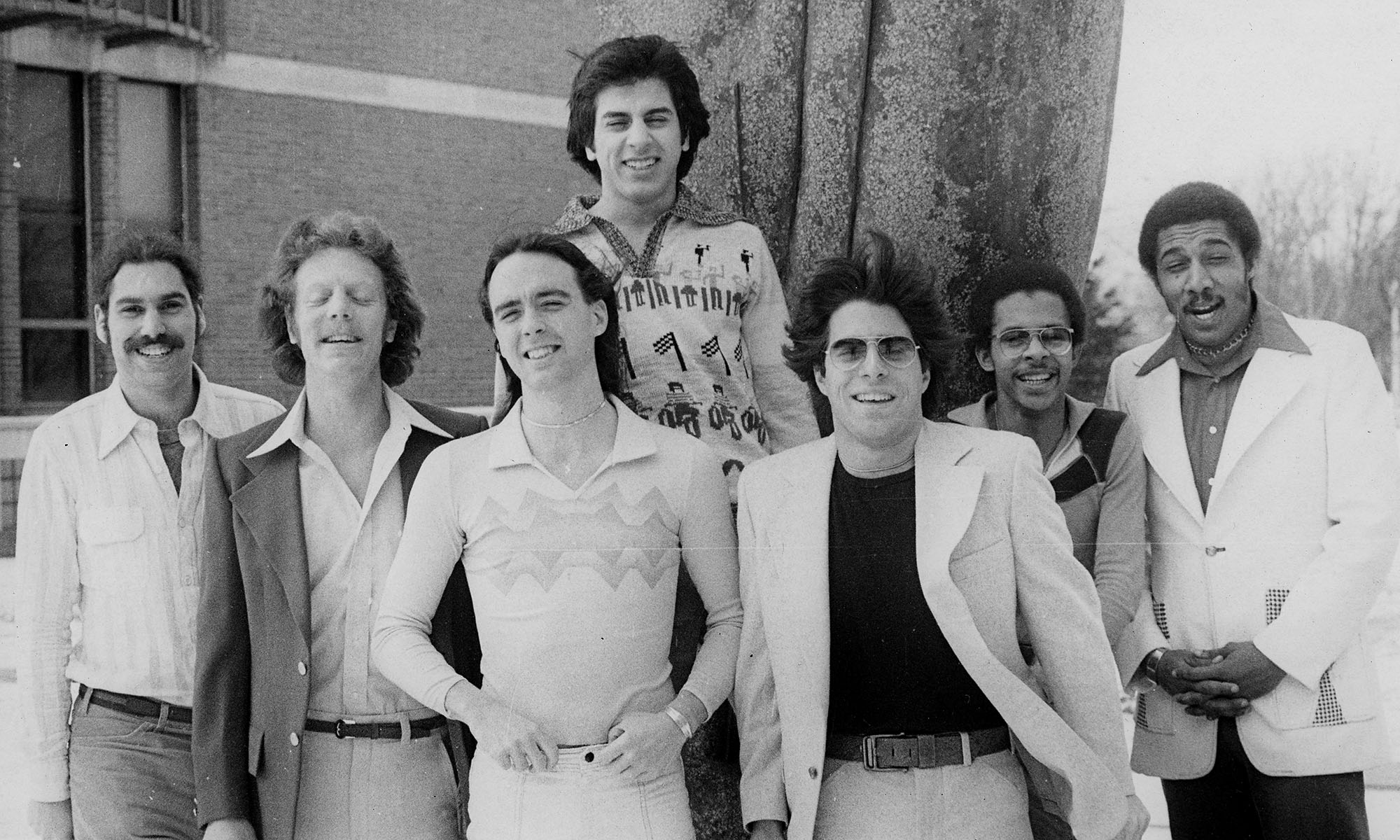 Black-and-white archival photo of the seven members of Broad Street Stroke posing together outdoors in 1970s attire.