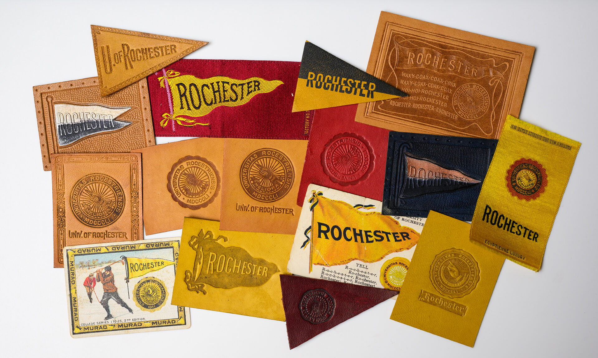 A group of leather and silk rectangles and pennants featuring the University of Rochester seal and name.