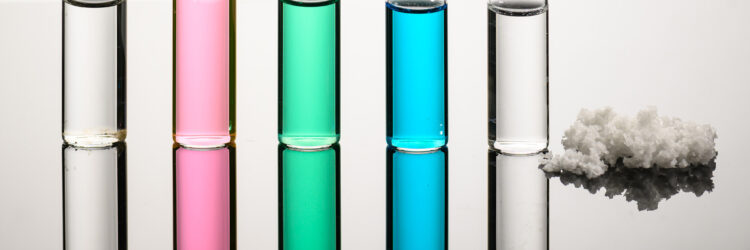 Five different colored vials holding seawater, Great Salt Lake water, nickel sulfate, copper chloride wastewater, and desalinated water standing next to a pile of salt.