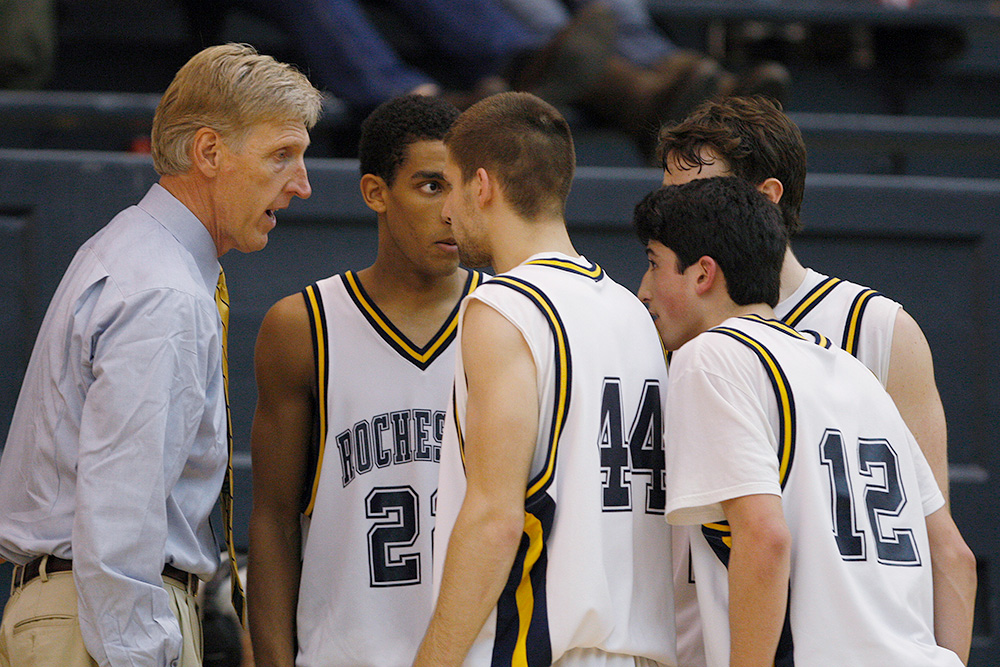 Coach Mike Neer addresses four Rochester players in a sideline huddle during a game.