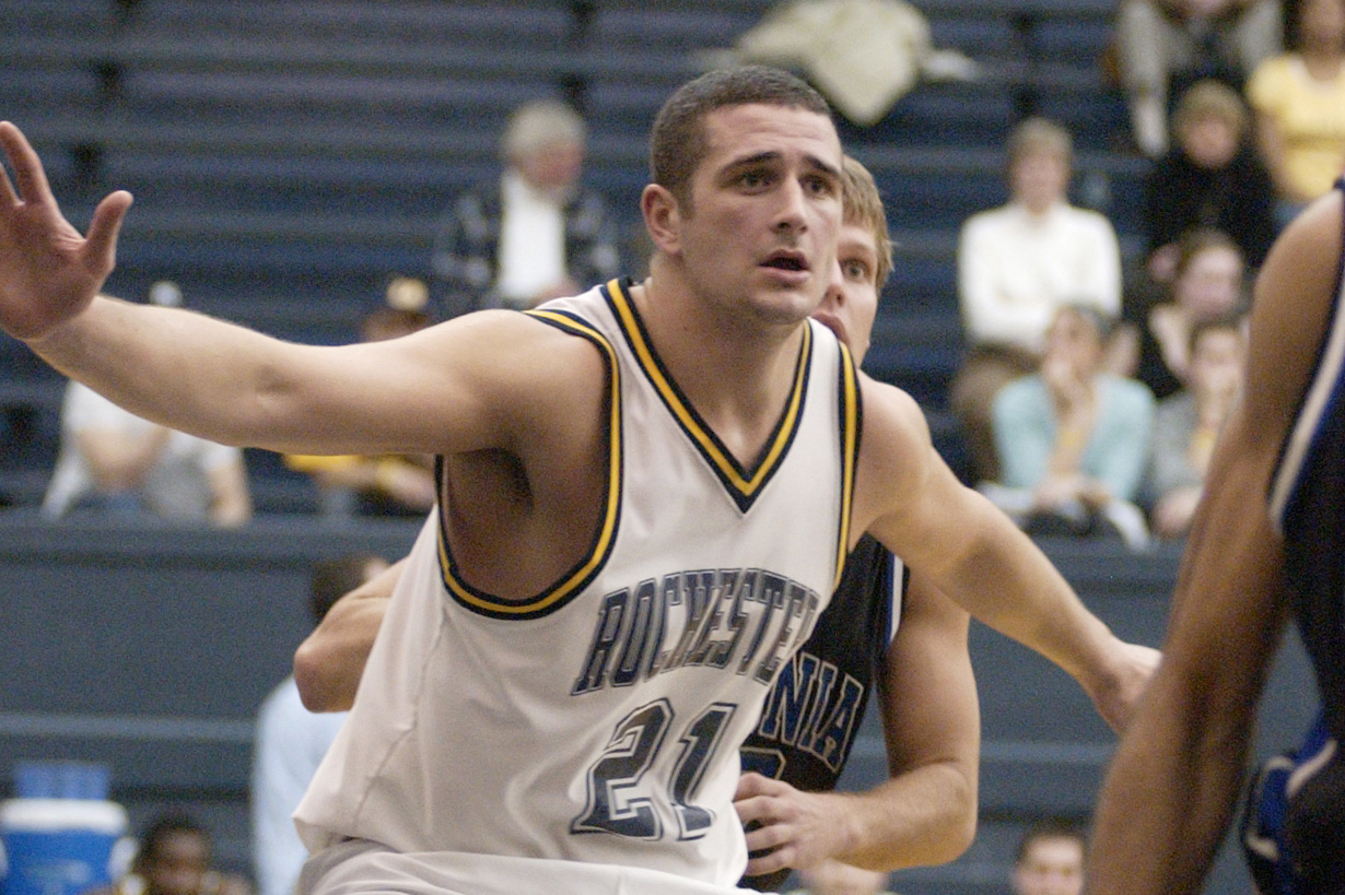 Rochester player Seth Hauben, wearing number 21, boxes out a defender during a game as spectators look on.