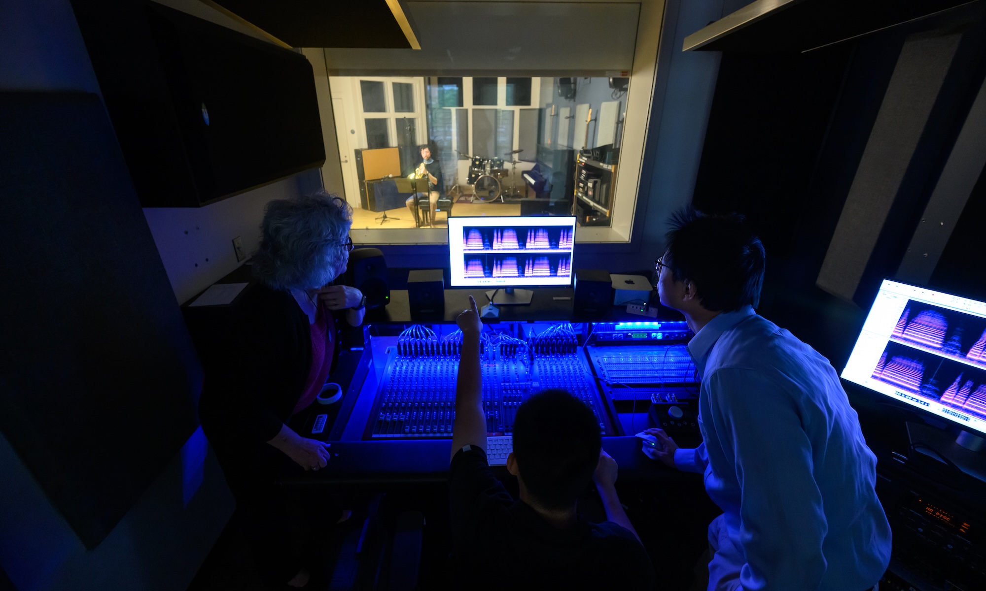 Three researchers look at a screen of analysis while French horn player Jacob Factor plays music wearing a custom neck brace to help address pharyngoceles.