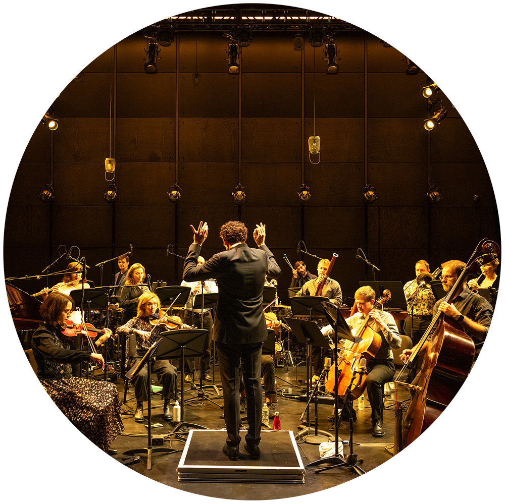 Circular crop of a photo of Alarm Will Sound performing on stage.