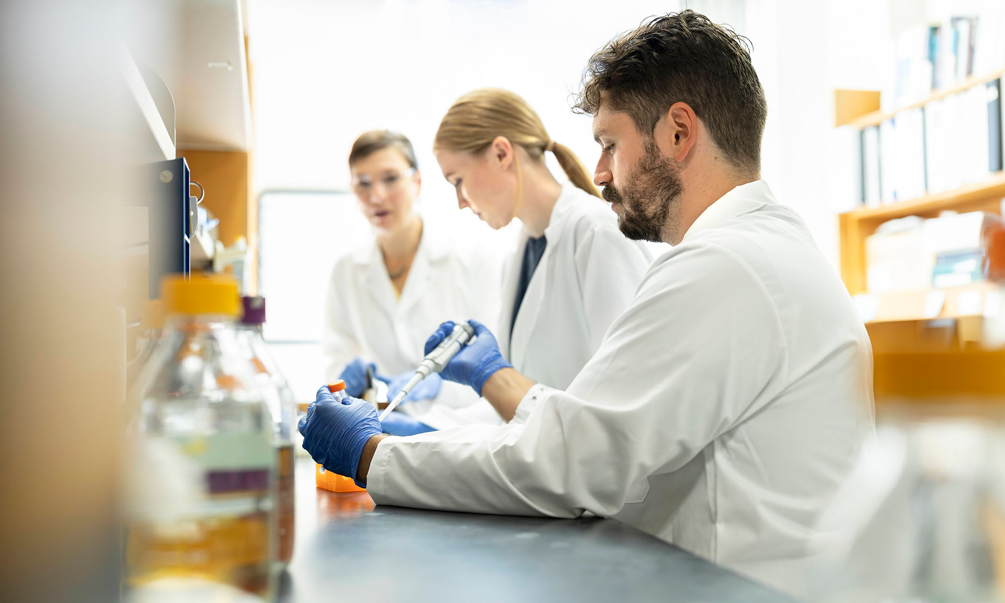 Three URochester researchers in lab coats working in a research laboratory.