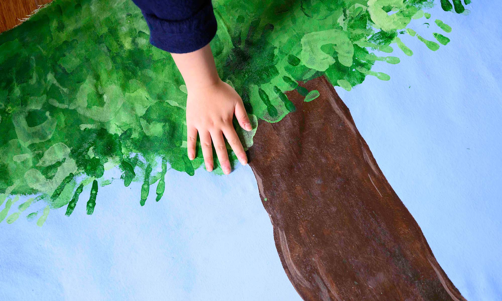 Overhead shot of a hand being placed on an artwork featuring a tree's leaves made of other handprints.