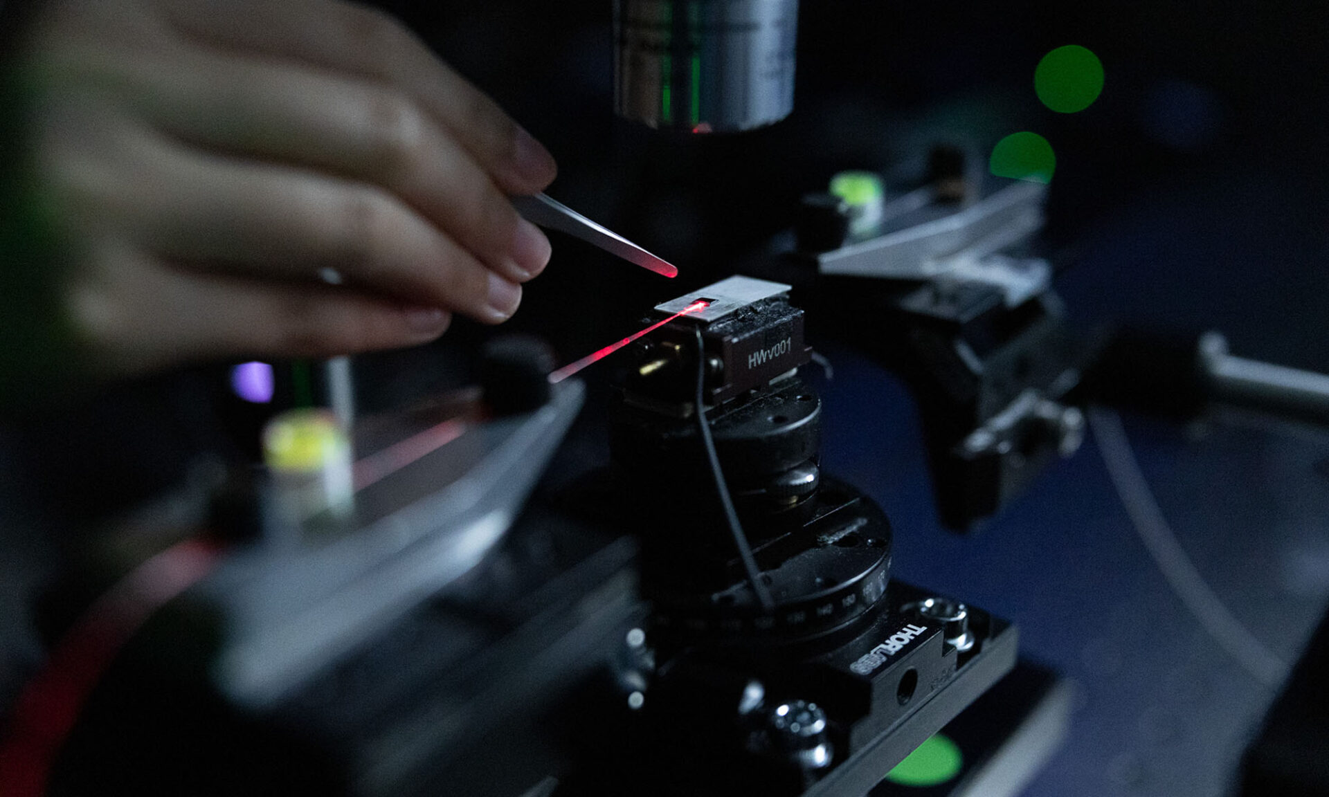 Close up of a hand holding an instrument near an apparatus emitting a red laser representing the kind of work and manufacturing supported by the NSF STELLAR Engine.