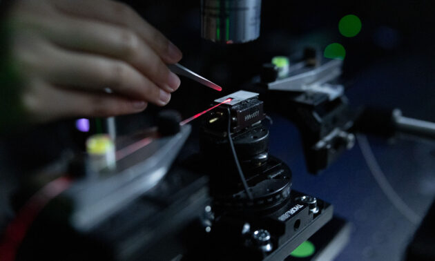 Close up of a hand holding an instrument near an apparatus emitting a red laser representing the kind of work and manufacturing supported by the NSF STELLAR Engine.