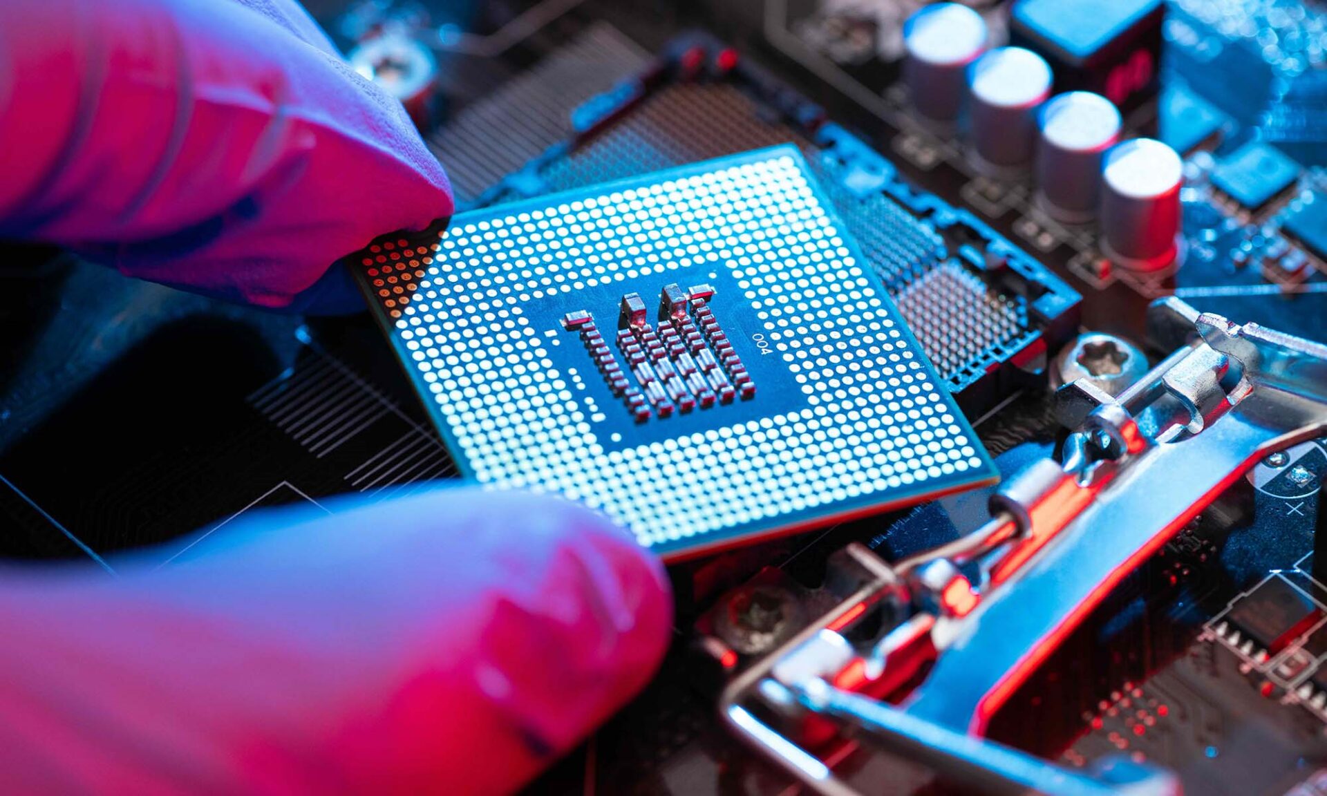 Close-up of gloved fingers holding a microchip near a circuit board.