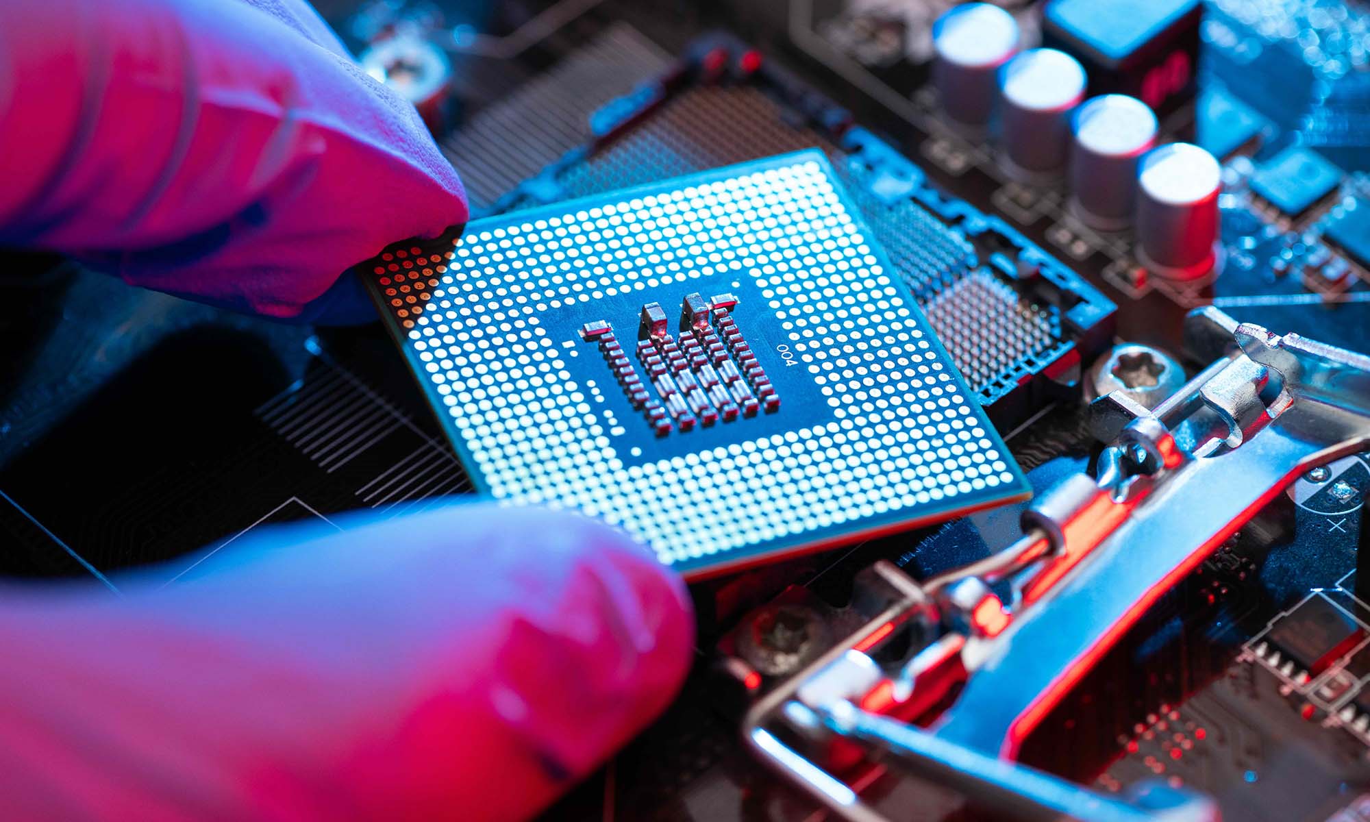 Close-up of gloved fingers holding a microchip near a circuit board.