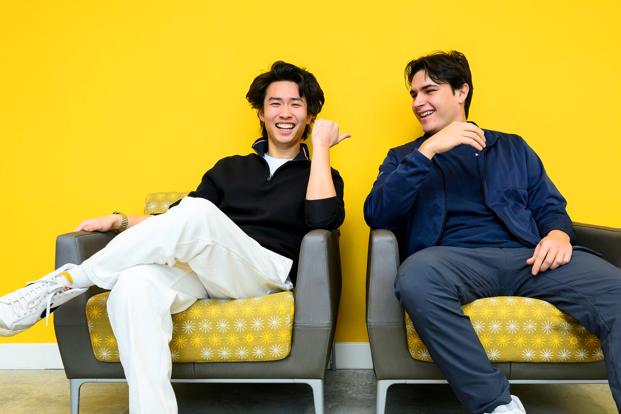 Stephen Lim and Walter McDonald seated casually in chairs with smiles on their faces against a bright yellow-colored background wall.