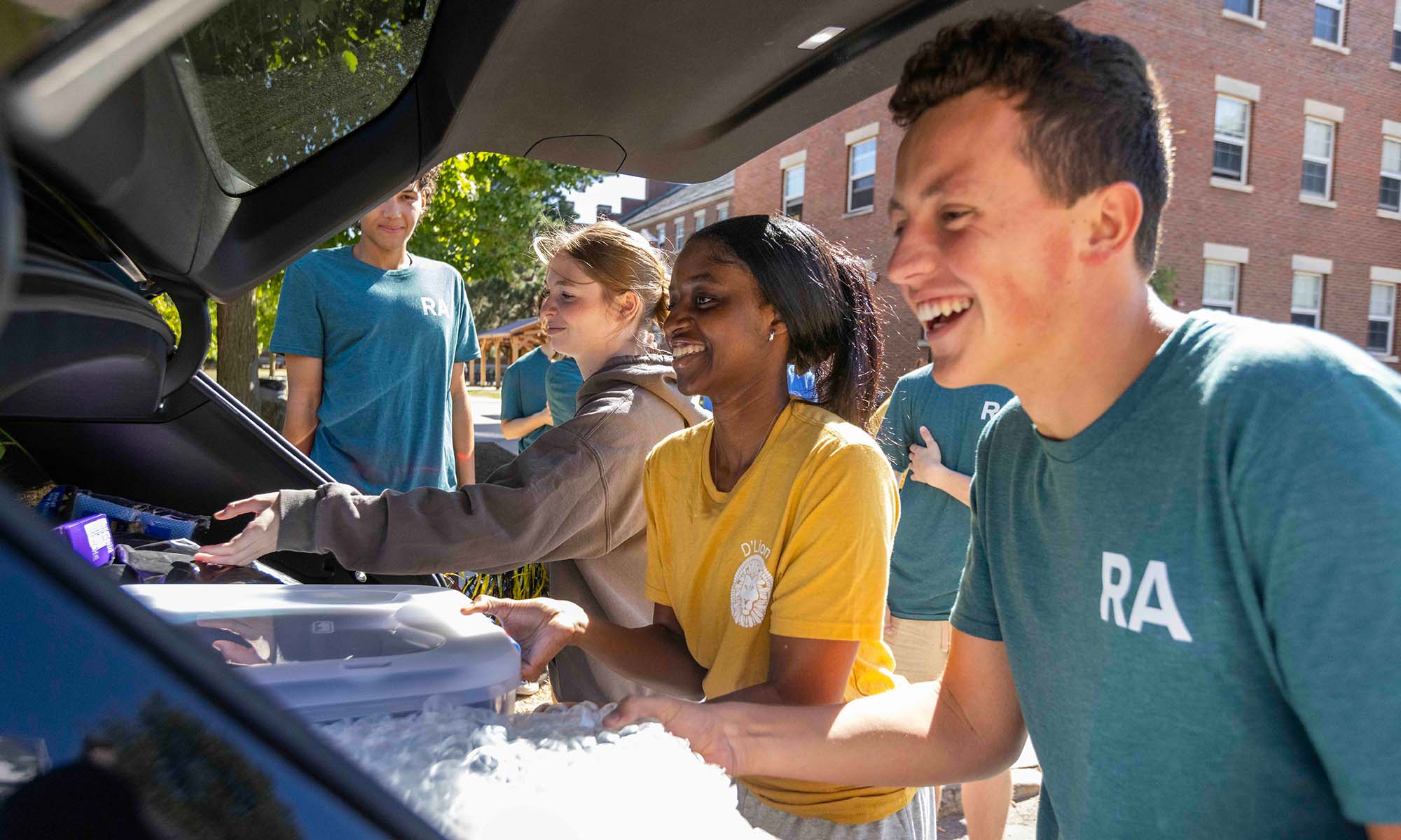 URochester students and RAs help new students unpack a car trunk full of college packing list essentials for the dorm.