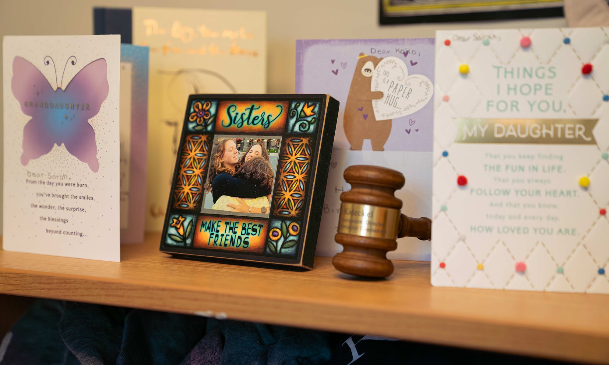 A shelf displaying greeting cards, a framed photo, and a gavel, items precious to Sarah Kideckel and part of her college packing list.
