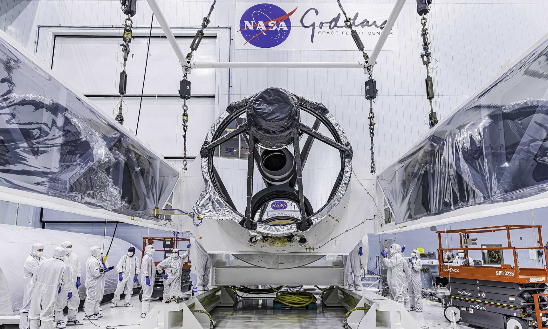 NASA’s Nancy Grace Roman Space Telescope suspended inside a large clean room at Goddard Space Flight Center as technicians work nearby.