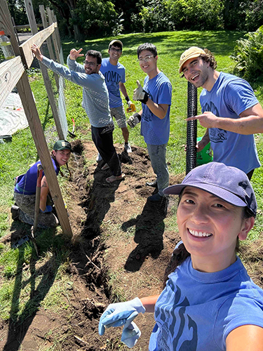 Incoming Simon MBA students in their purple orientation shirts pose for a group selfie while doing volunteer yardwork in the community.