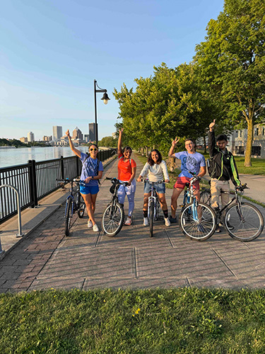 Five Simon Business School MBA students on bicycles near the Genesee River pathway.
