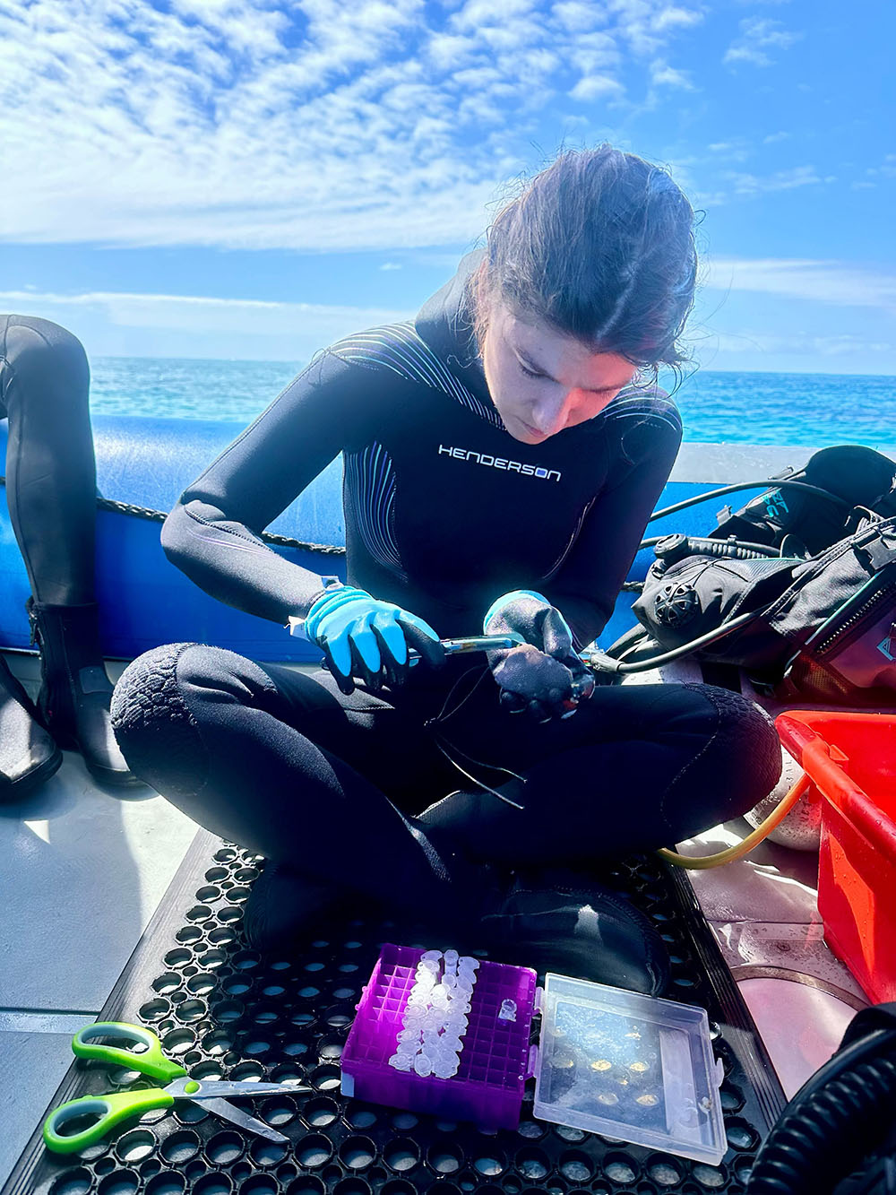 Marcelina Martynek sits cross-legged on a boat and examines a coral reef sample.
