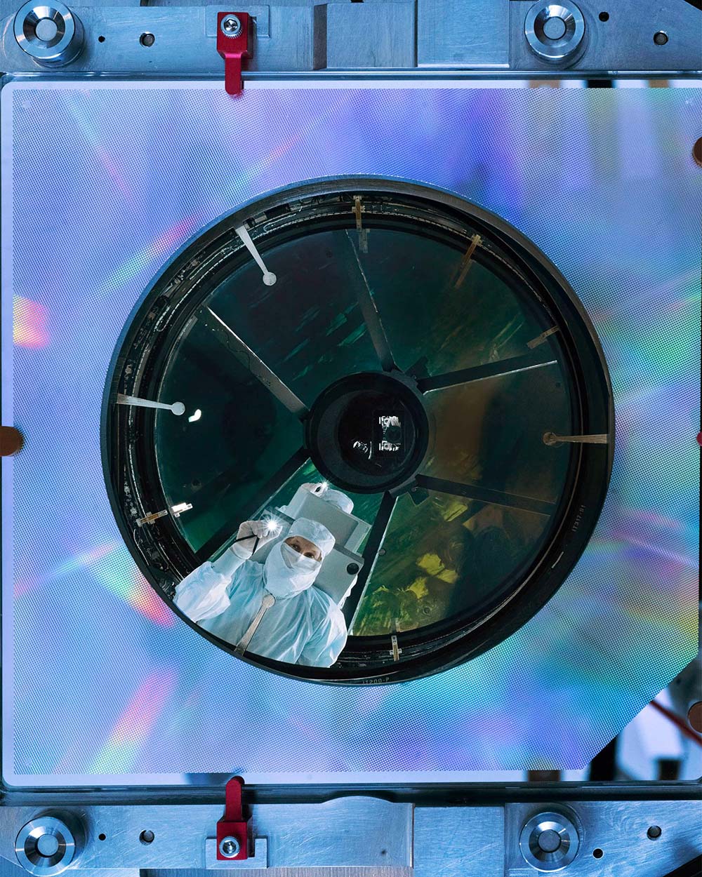 Close-up view into the mirrors and reflective surfaces of the Nancy Grace Roman Space Telescope's Imaging Optics Assembly with a person in a bunny suit looking down directly at the camera.