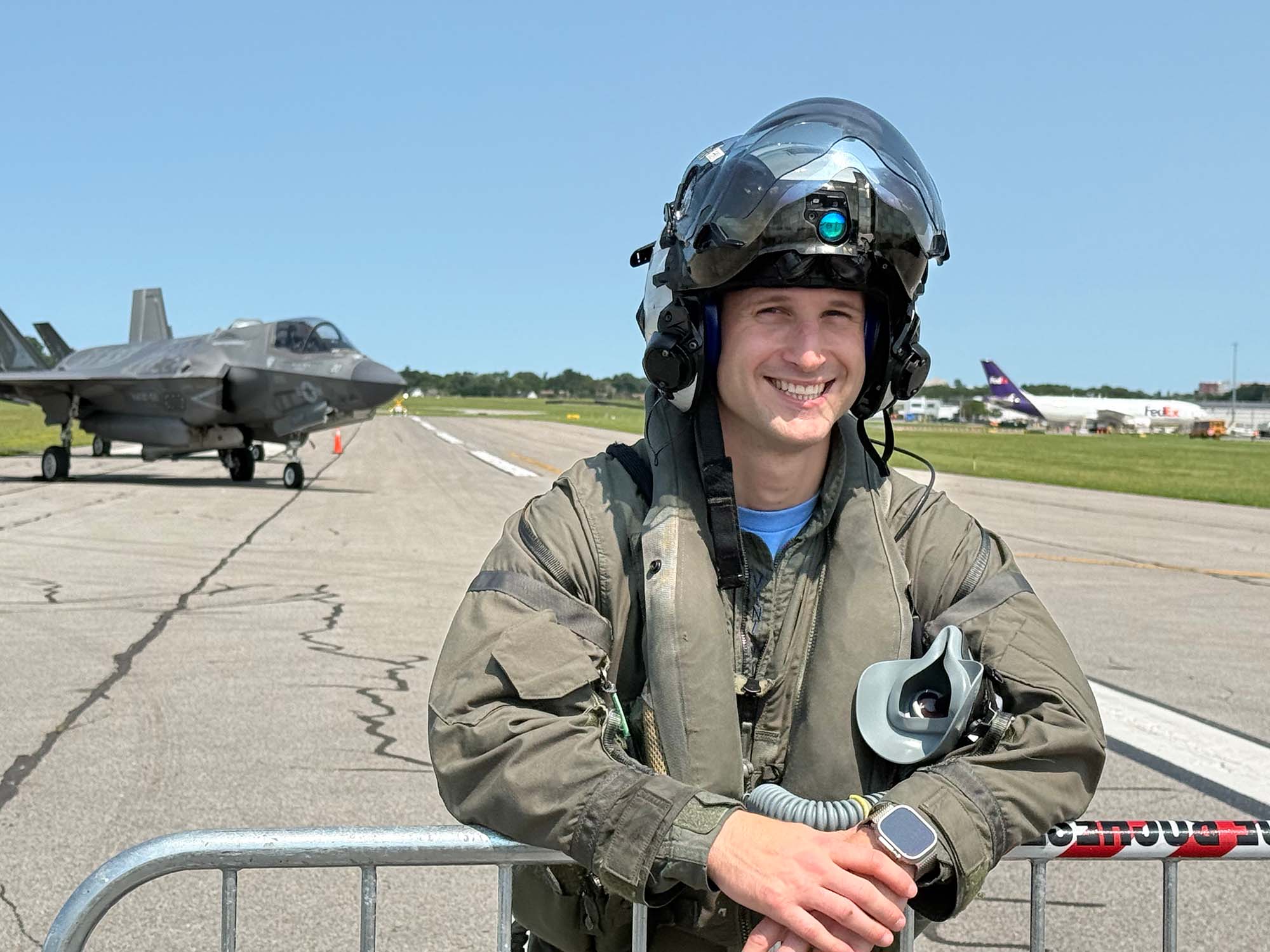 William Horn in a flight suit and helmet smiling with a jet behind him.
