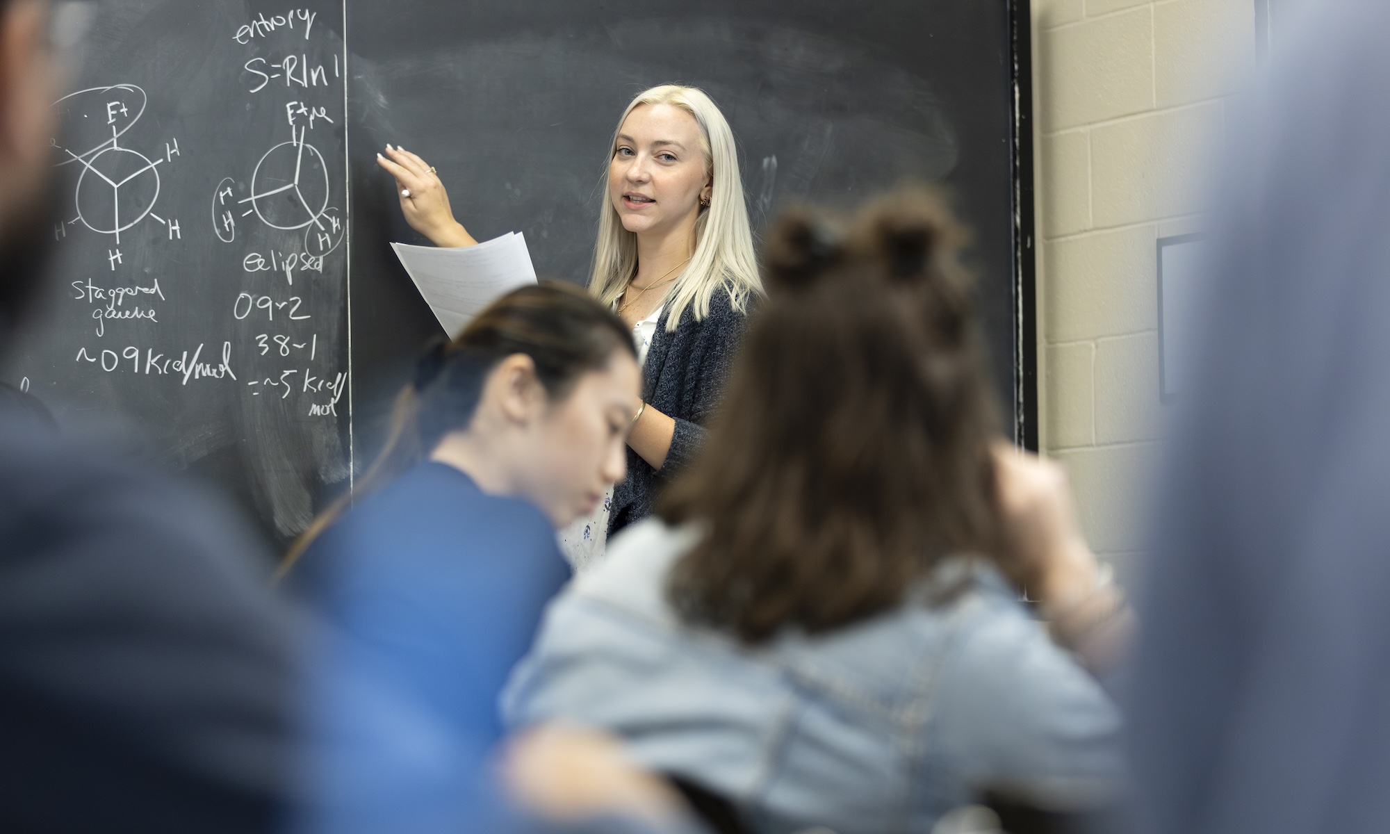 A professor writes on the chalkboard while students take notes.