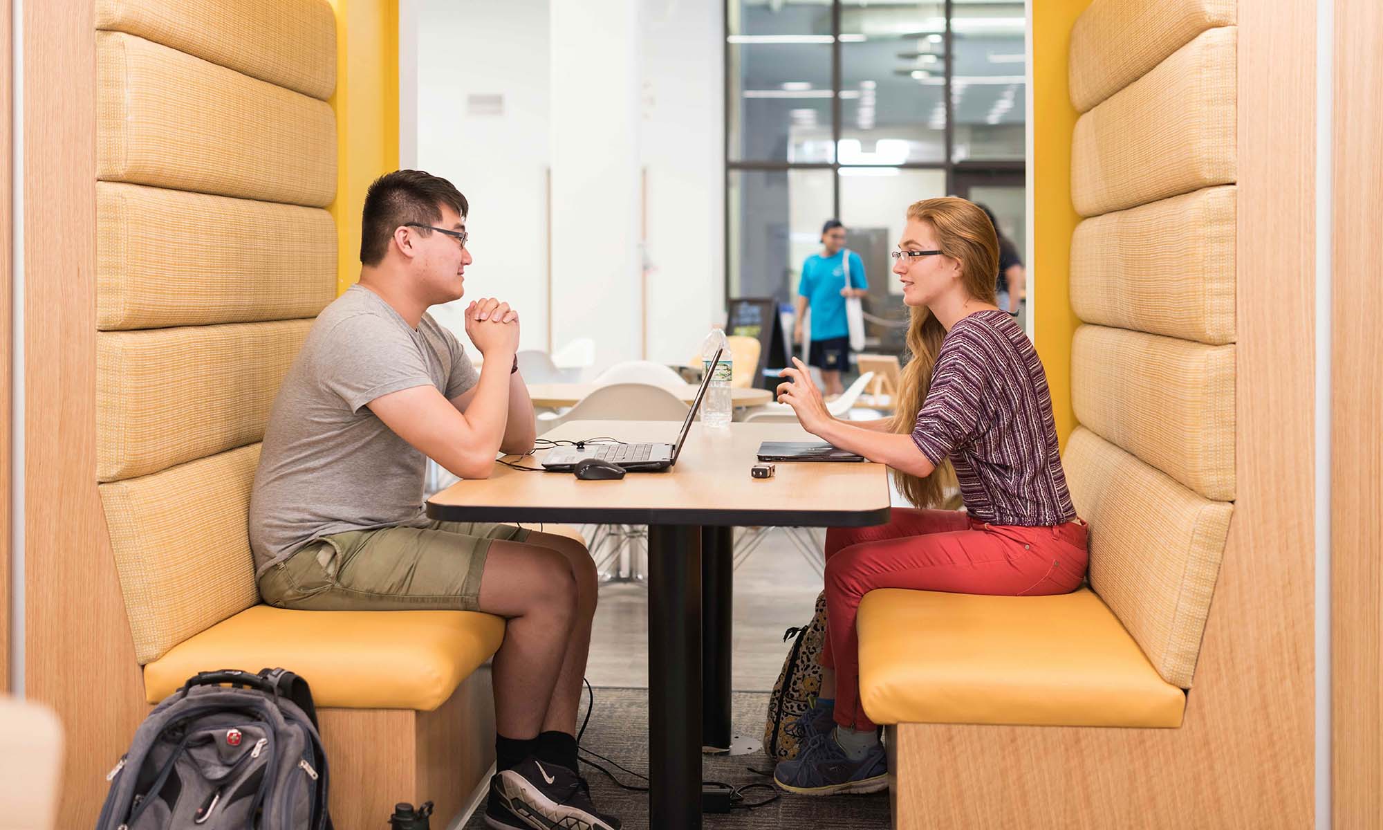 Two URochester students model what it looks like to be a good student by studying together in a booth at the iZone.