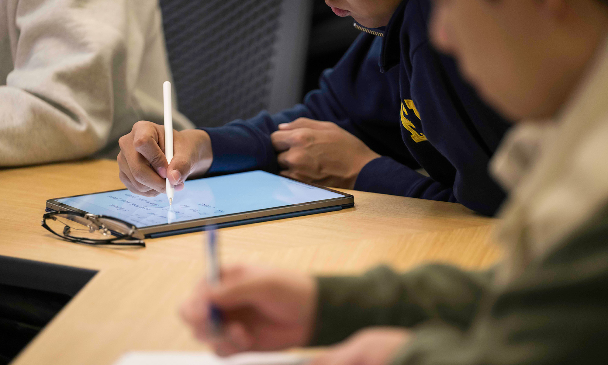 Close up of students taking notes during class on an electronic notebook.