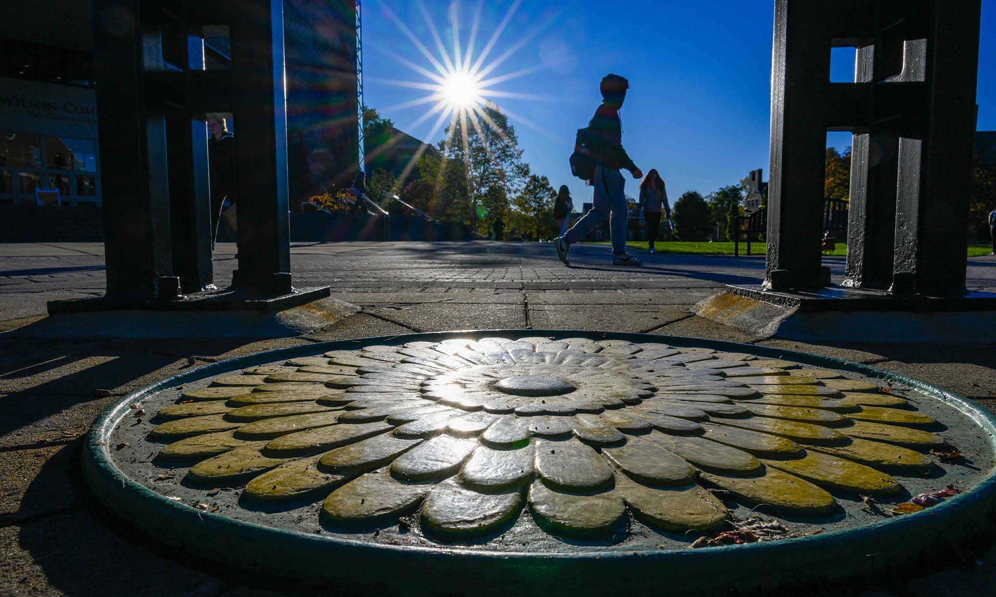 University of Rochester students walking on the Wilson Quad as seen from a low angle that shows the dandelion architectural detail under the Clock Tower.