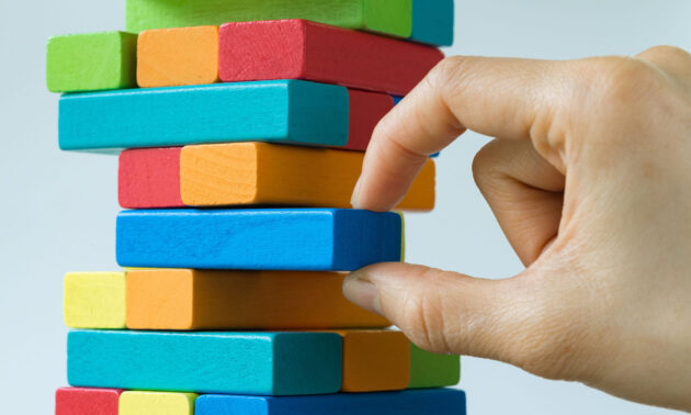 Close-up of a hand pulling out a blue colored block from a Jenga-like stack of colorful blocks to illustrate the removal of the cGAS protein from cells.