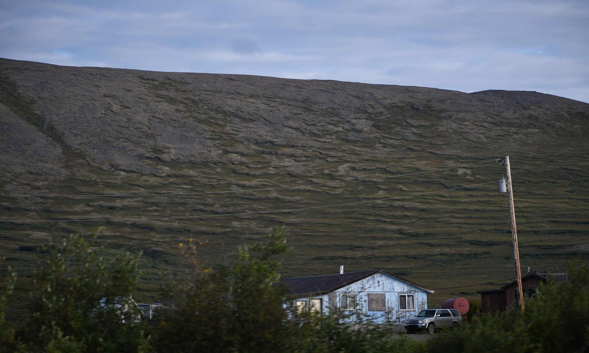 Solifluction-formed wave patterns on an Alaskan hillslope with a house a pickup truck at the base.