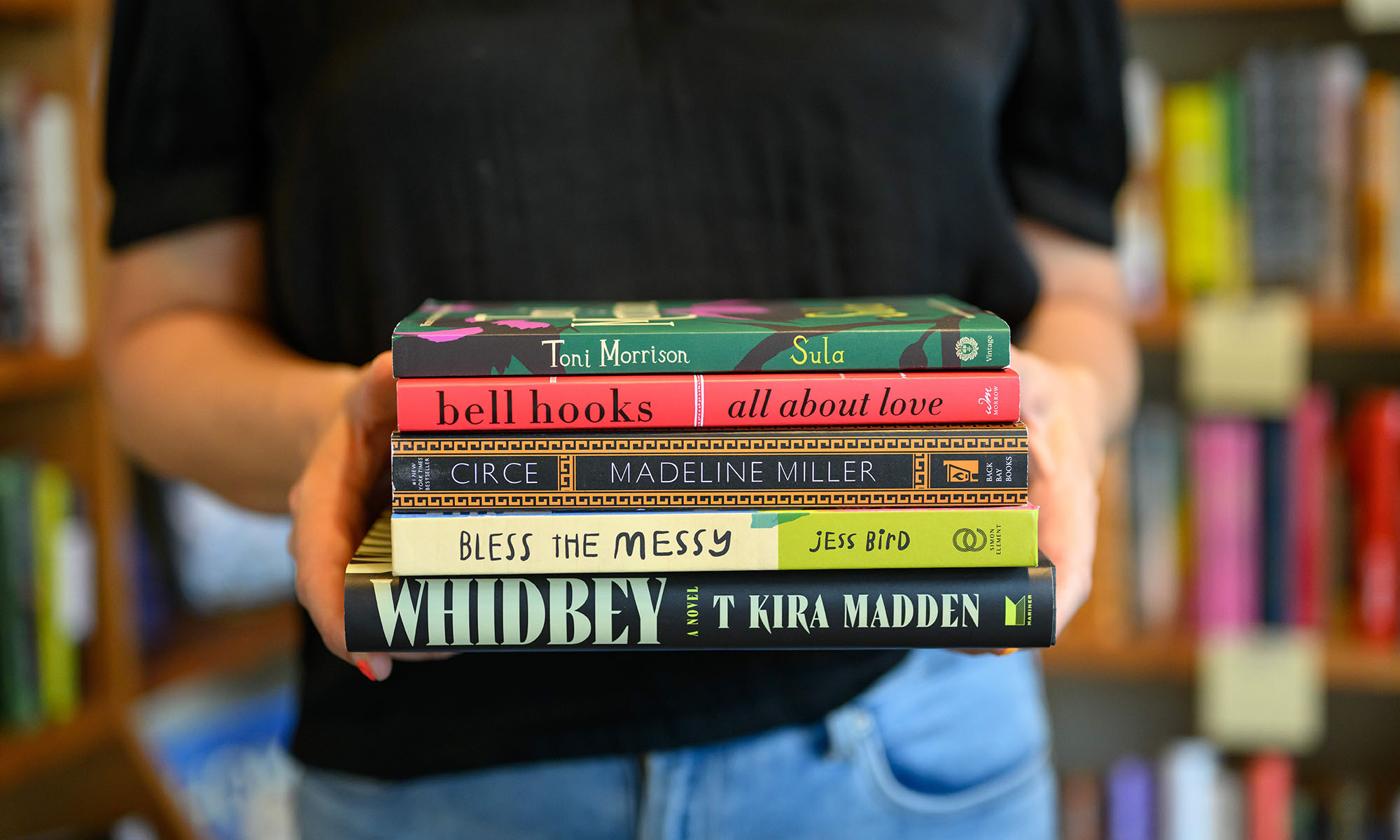 Siren and Sea owner Jess Gale holding five recommended books by Toni Morrison, bell hooks, Madeline Miller, Jess Bird, and T Kira Madden